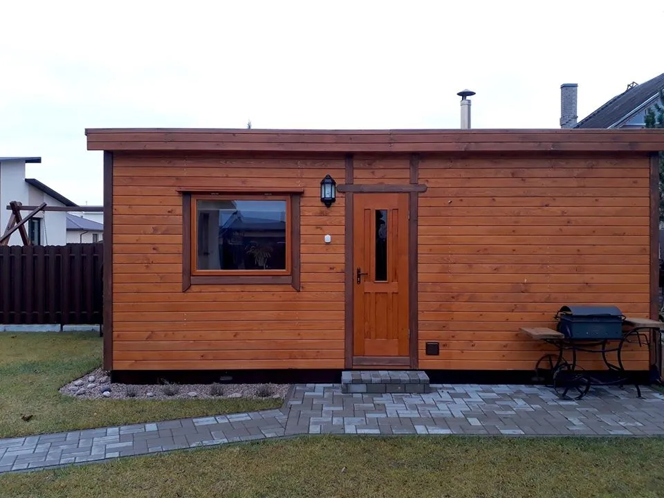 A timber-framed Latvian sauna standing on a lawn, with the door open